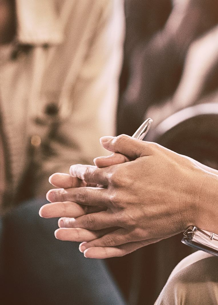 a seated female psychotherapist with clasped hands talking to another person