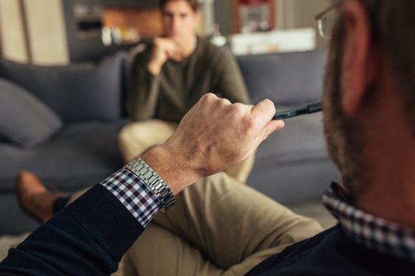 a male psychotherapist sitting on a sofa while holding a pen in his hand