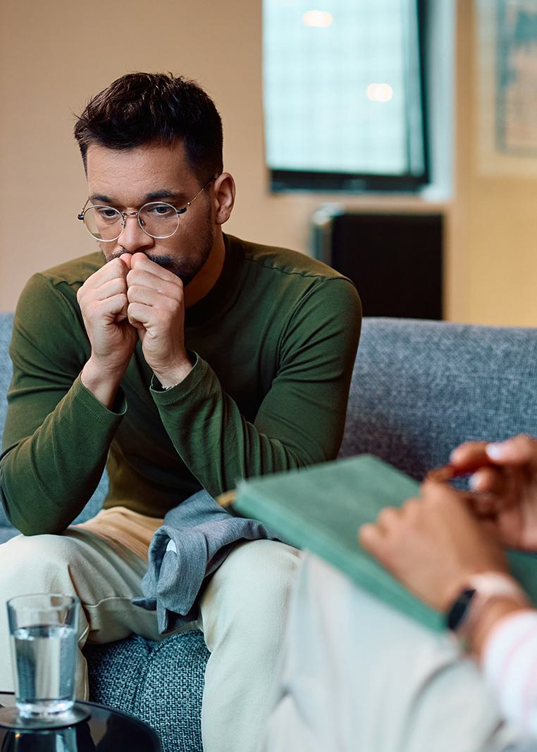 a young man looking thoughtful sitting on a sofa talking to a pychotherapist